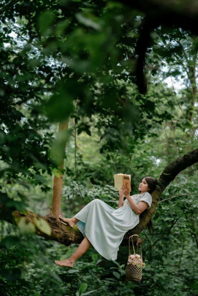 Eine Frau liest entspannt ein Buch, sitzend auf einem großen Ast in einem grünen Wald, als Symbol für das Finden von innerer Ruhe und das Überwinden der Angst vor der Angst.