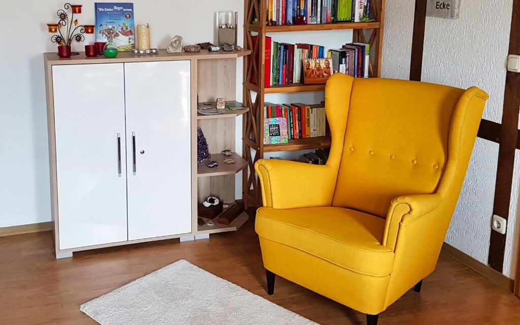 Einladende Beratungsecke mit gelbem Sessel und Fachliteratur in der Praxis für Hypnosetherapie Rudolstadt.
