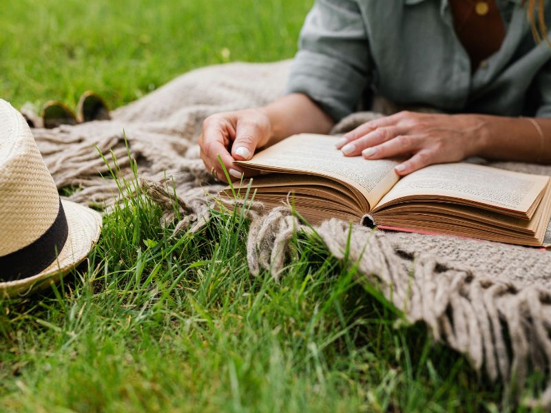 Eine Person liest entspannt ein Buch auf einer Wiese. Ein Symbolbild für gelungene Stressbewältigung Rudolstadt.