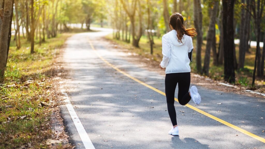 Fokussierte Frau joggt auf einem sonnigen Waldweg, passend zum Thema Mentales Coaching und Zielausrichtung im Sport.
